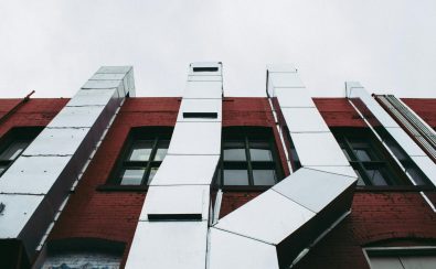 Low angle view of a modern industrial facade with prominent metal ducts on a red brick building.