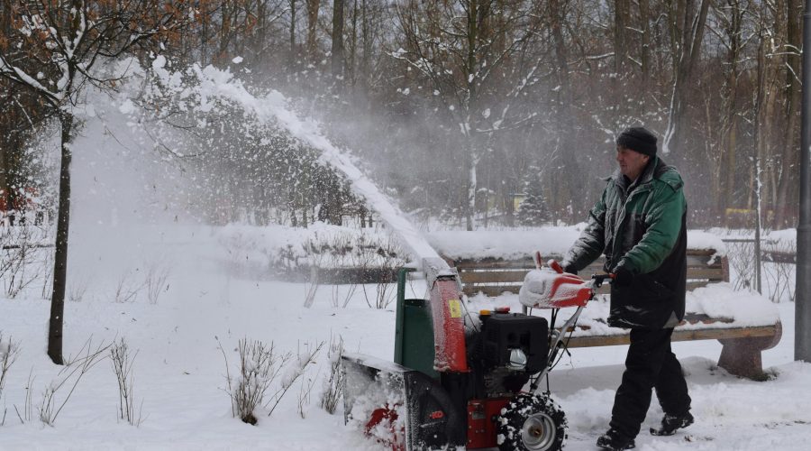 A man uses a snow blower in a snowy park during wintertime.